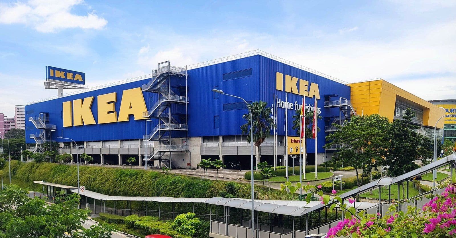 The blue and yellow IKEA Tampines store in Singapore, seen from a raised walkway above the road to its car park entrance.