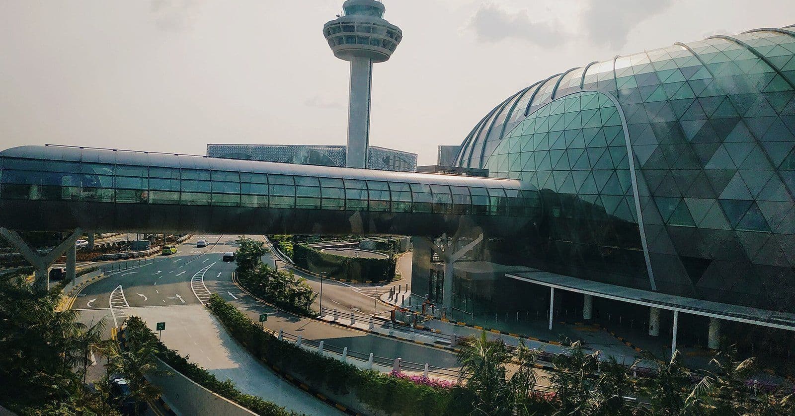 The glass dome of Jewel Changi Airport in Singapore beside the airport control tower, with the access roads in front.