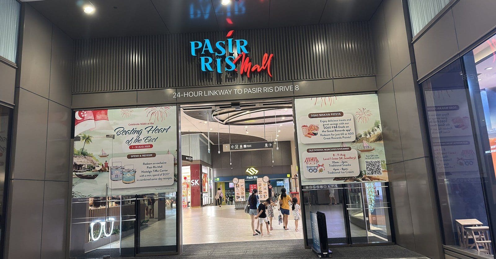 The entrance to Pasir Ris Mall in Singapore, with the mall's name above the doors and shoppers walking inside.